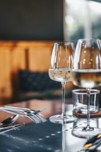 Two people toasting with wine glasses over a table set with diverse dishes, including cheese, vegetables, and bread.