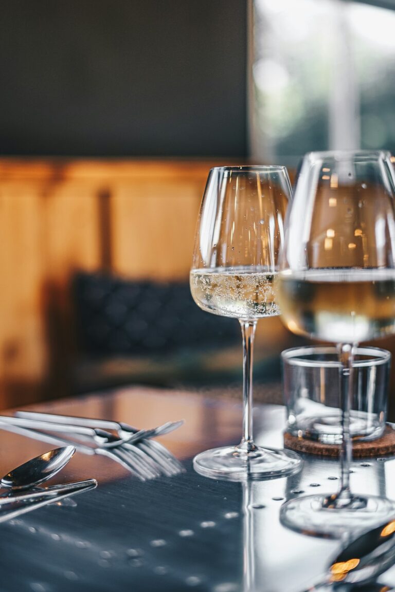 Two people toasting with wine glasses over a table set with diverse dishes, including cheese, vegetables, and bread.
