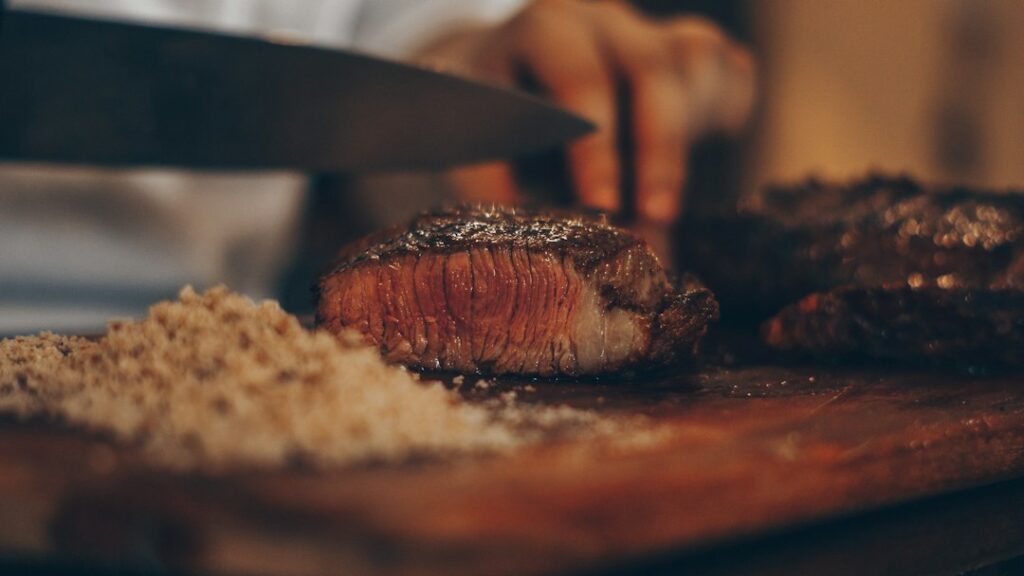 Sliced medium-rare steak resting beside a hot skillet, tongs, herbs, and a thermometer
