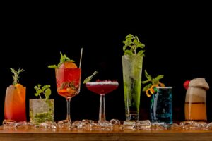 Four adults at a restaurant table with colorful non-alcoholic drinks garnished with fruit and herbs.